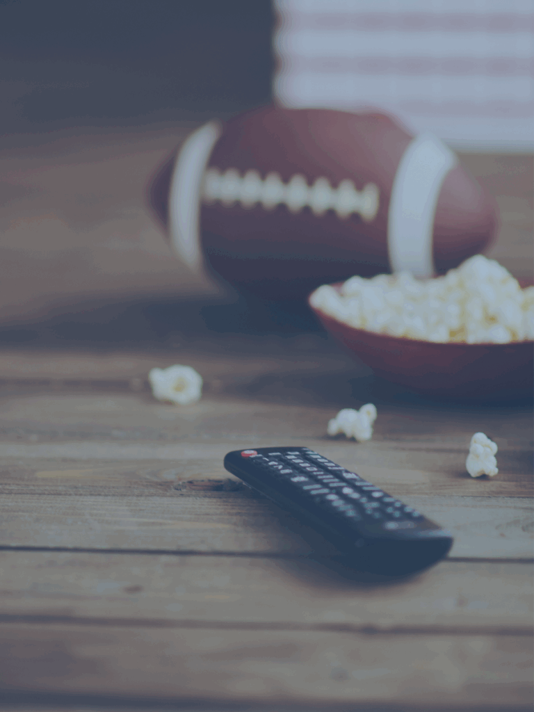 Remote on table with a football and popcorn in the background.