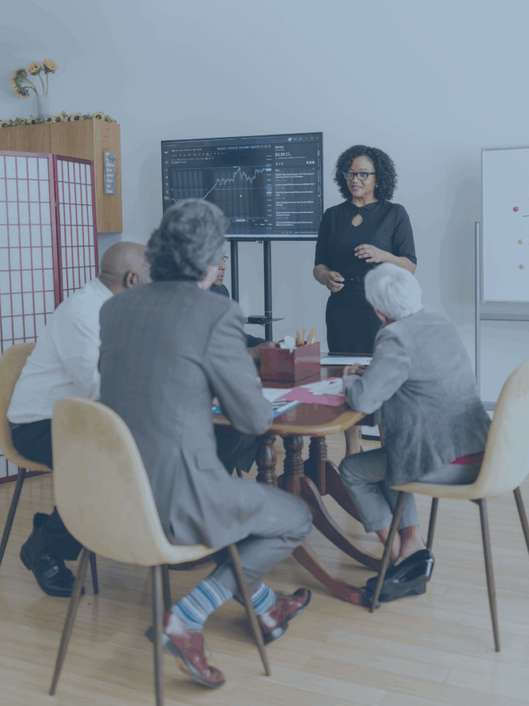 Woman standing and showing a screen with data to a table of men.