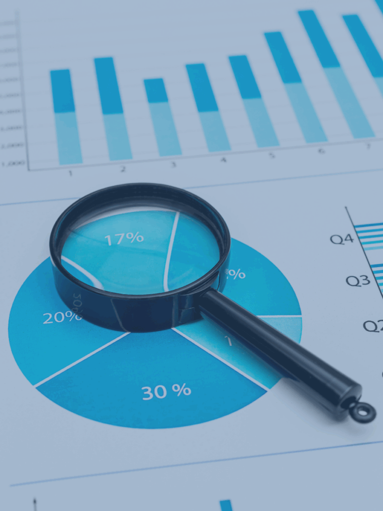 Magnifying glass laying on top of blue graphs and charts.