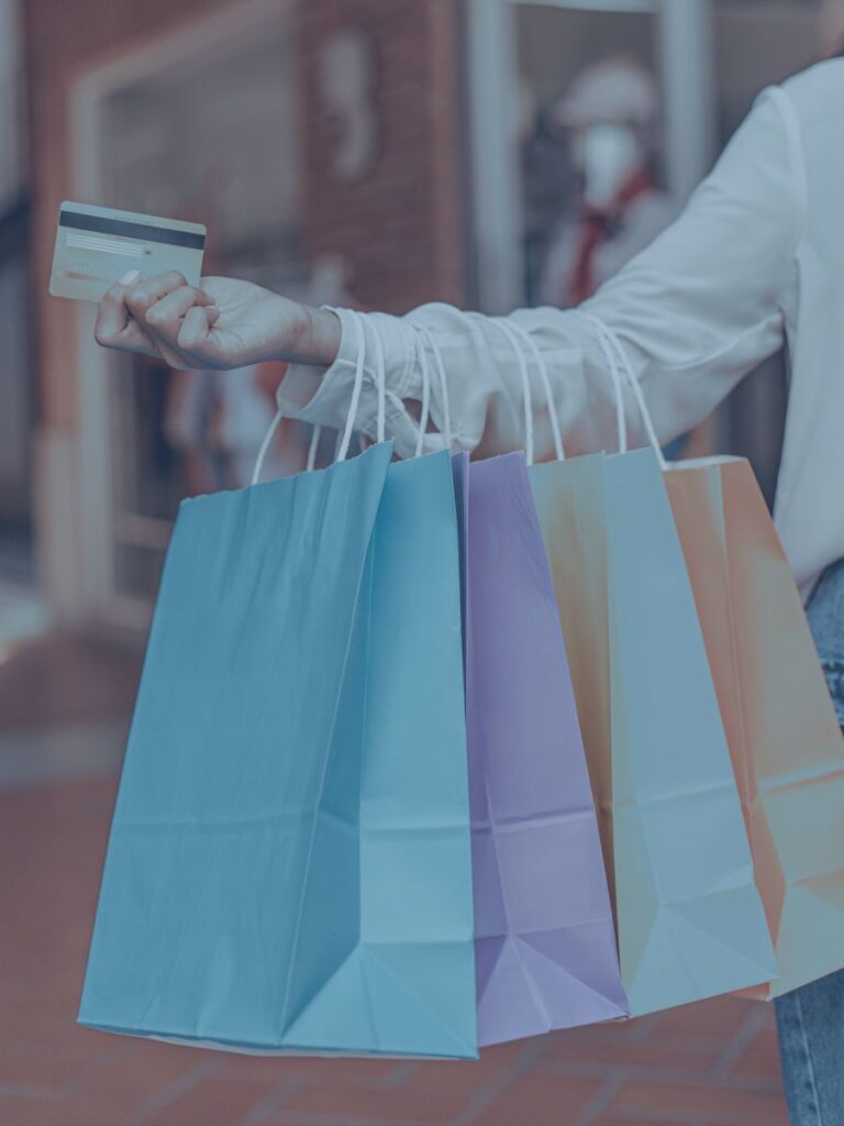 Arm of human holding shopping bags and a credit card in her hand.