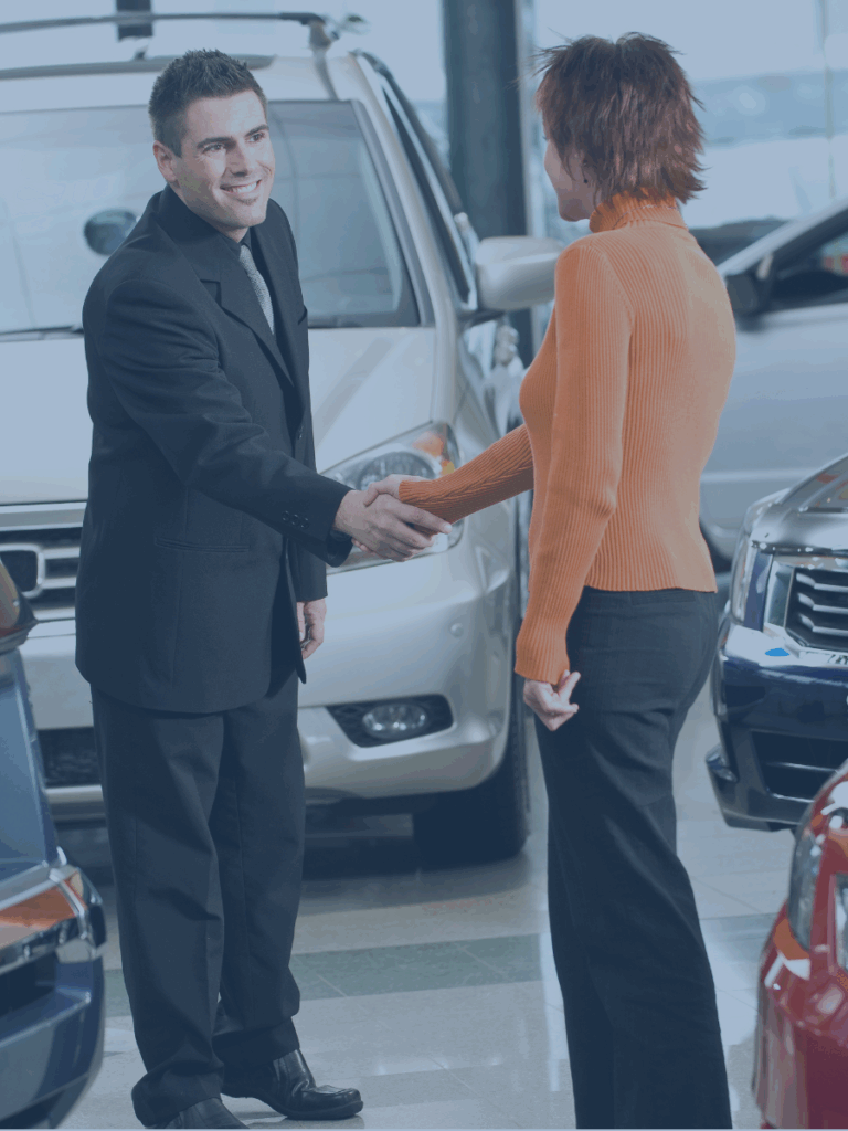 Two humans shaking hands in a car dealership.