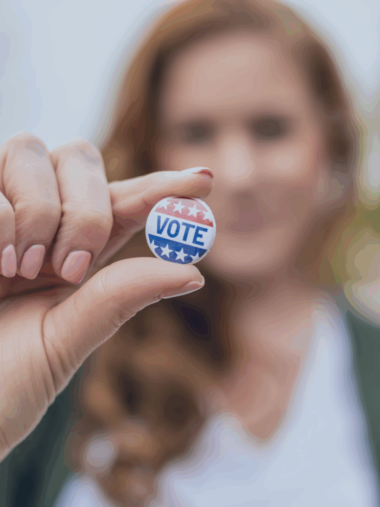 Human holding out a pin that says vote.